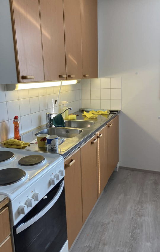 Elina's clean kitchen with a stove, stainless-steel sink and wooden cupboards